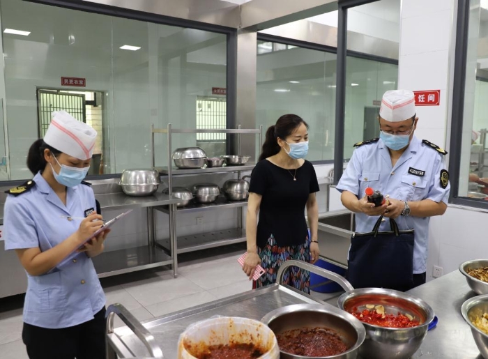 圖為執(zhí)法人員在檢查學(xué)校食堂加工制作情況。