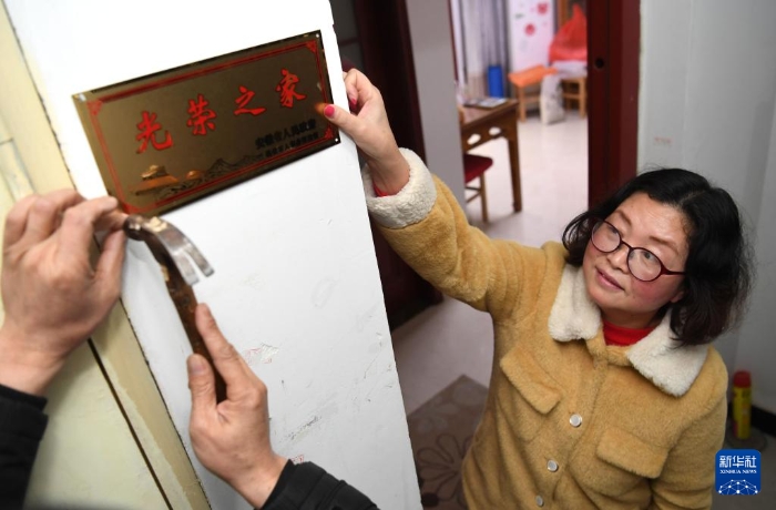 合肥市包河區(qū)常青街道工作人員在居民魏松梅（右）家門口懸掛“光榮之家”牌（2019年1月14日攝）。新華社記者 劉軍喜 攝